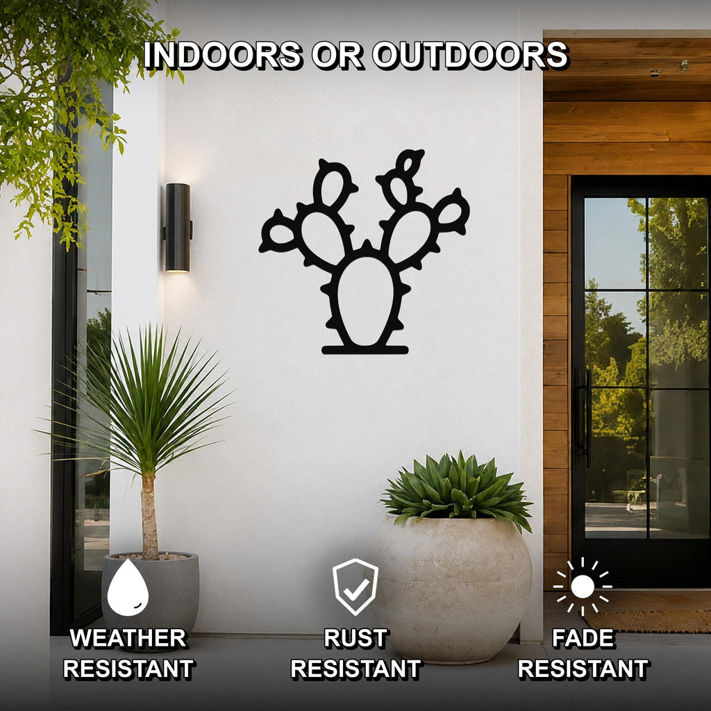 Black metal prickly pear cactus wall art with cutout spines and pads, mounted on a white exterior wall beside a glass door and potted plants.