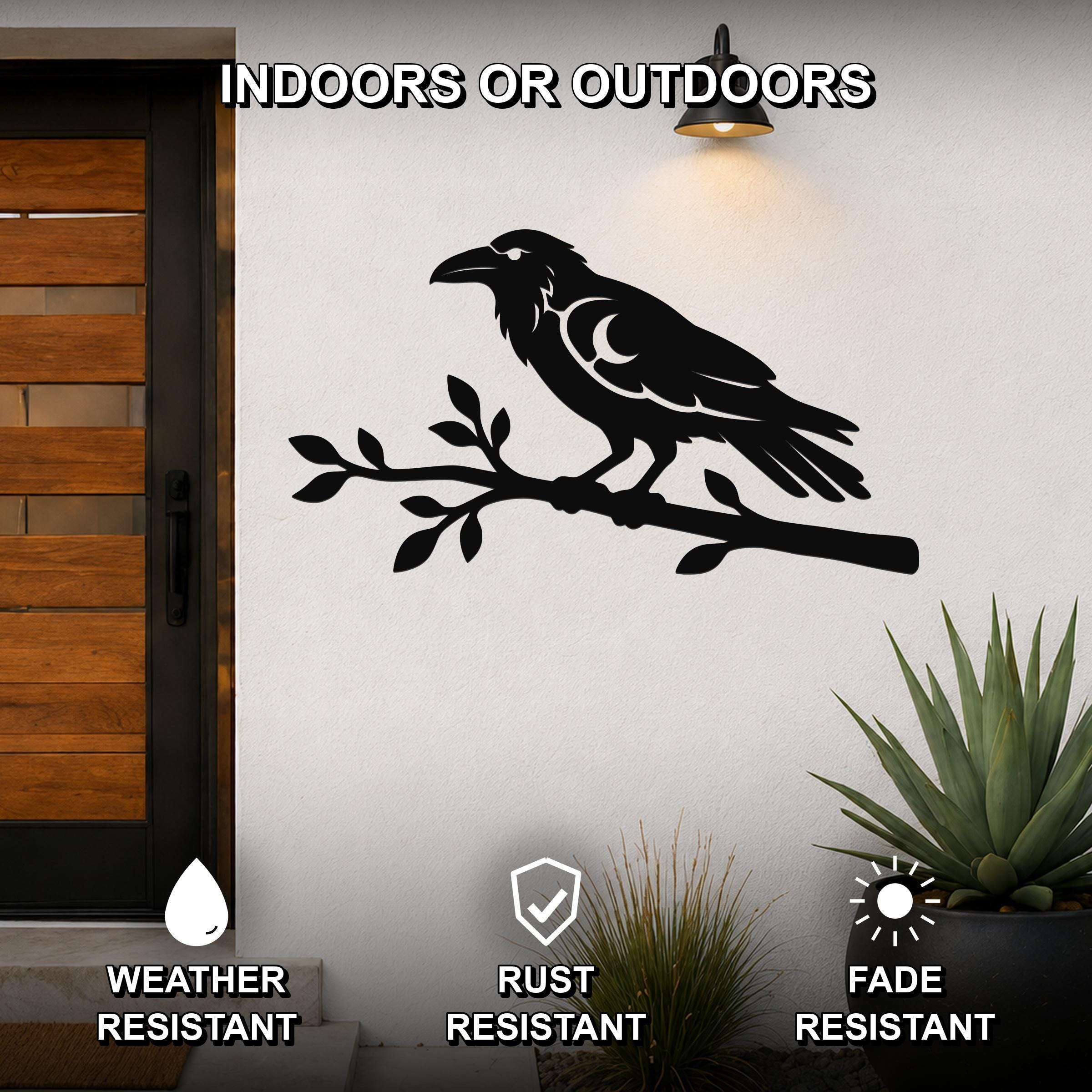 Black metal raven wall art with a crescent moon cutout, perched on a branch, mounted on an outdoor wall beside a wooden door.
