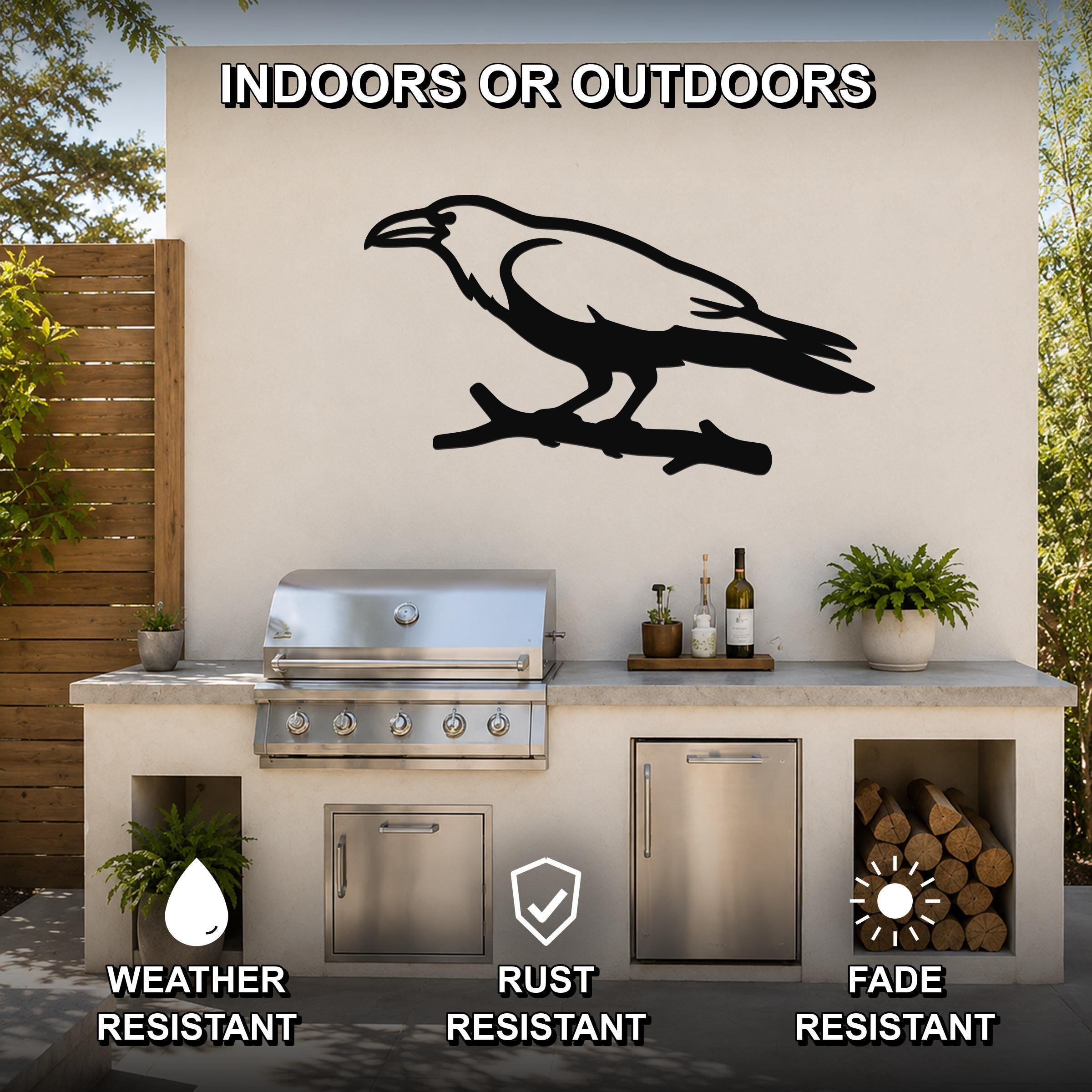 Black metal raven wall art silhouette perched on a branch, mounted on an outdoor kitchen wall above a stainless steel grill.
