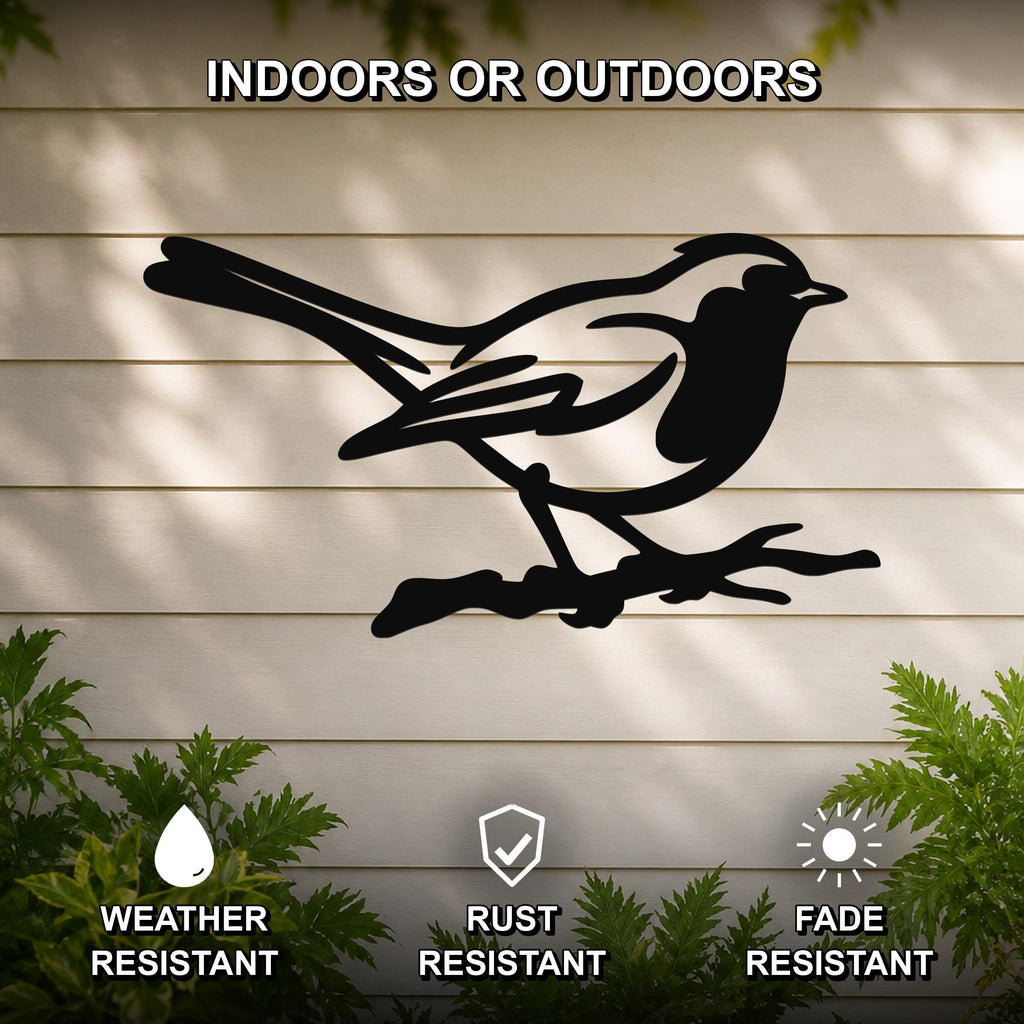 Black metal bird wall art silhouette perched on a branch, mounted on a light-colored outdoor wall with greenery, weather resistant, rust resistant, and fade resistant.