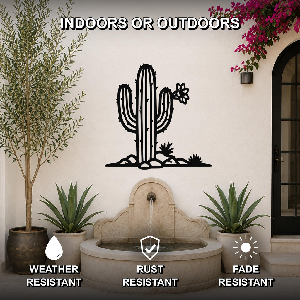 Black metal saguaro cactus wall art with flower and rock cutouts, mounted on an outdoor wall above a stone fountain in a patio setting.