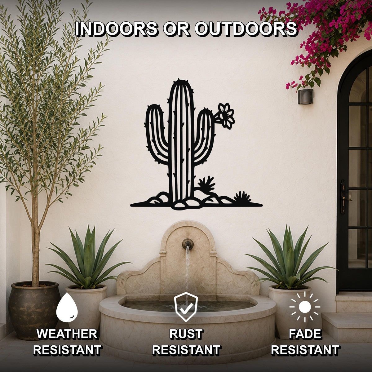 Black metal saguaro cactus wall art with flower and rock cutouts, mounted on an outdoor wall above a stone fountain in a patio setting.