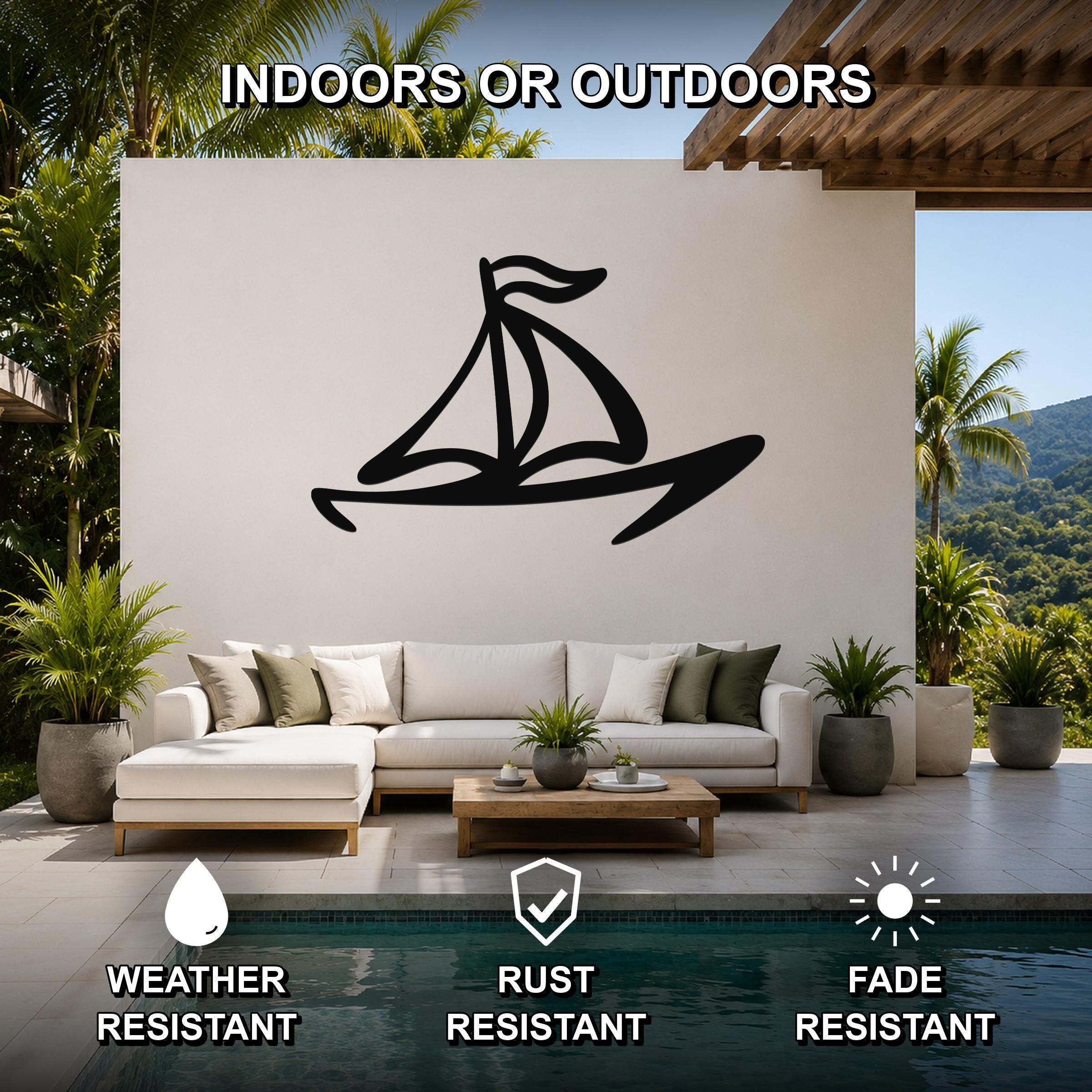 Black metal sailboat wall art with bold lines and a flag cutout, mounted on a white outdoor wall above a sofa in a patio living area.