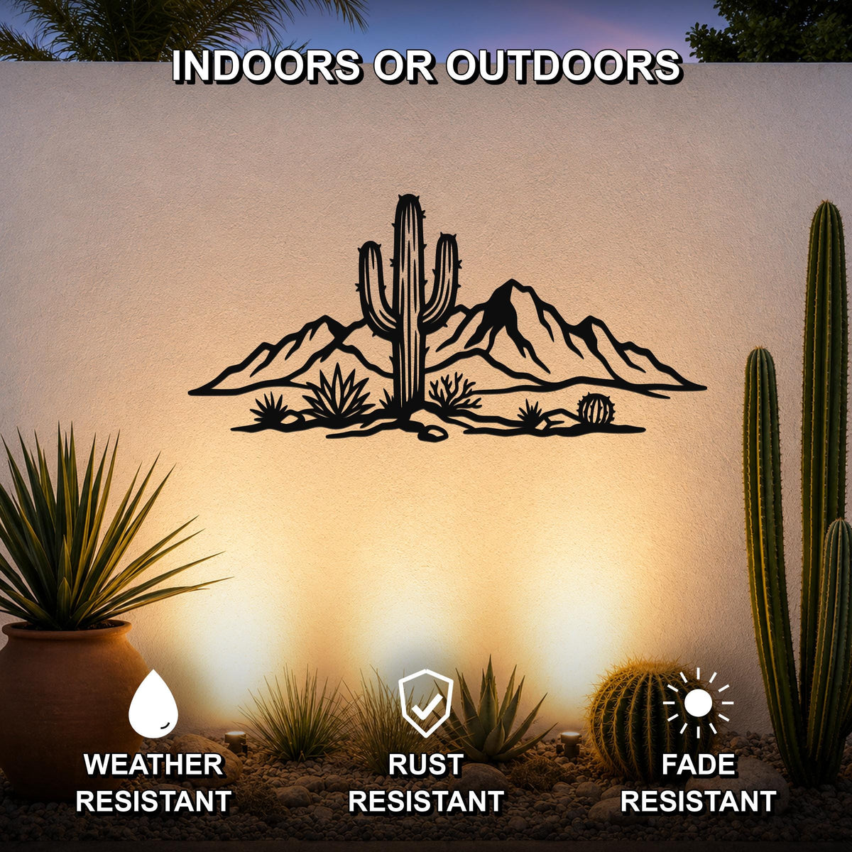 Black metal wall art featuring a desert landscape silhouette with a saguaro cactus and mountains, mounted on an outdoor wall above a gravel garden with potted cacti.
