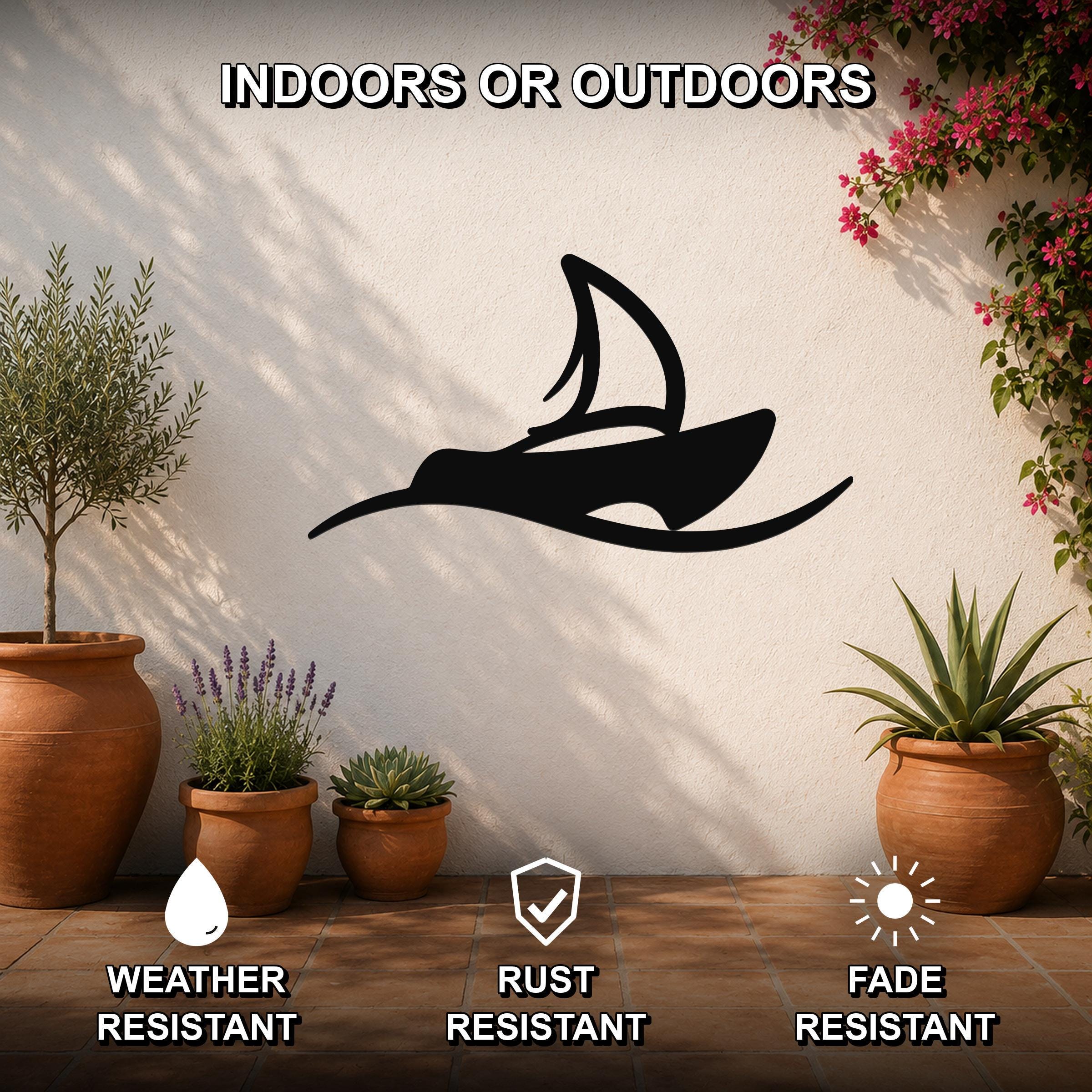 Black metal sailboat wall art with a silhouette design, mounted on an outdoor patio wall above potted plants.