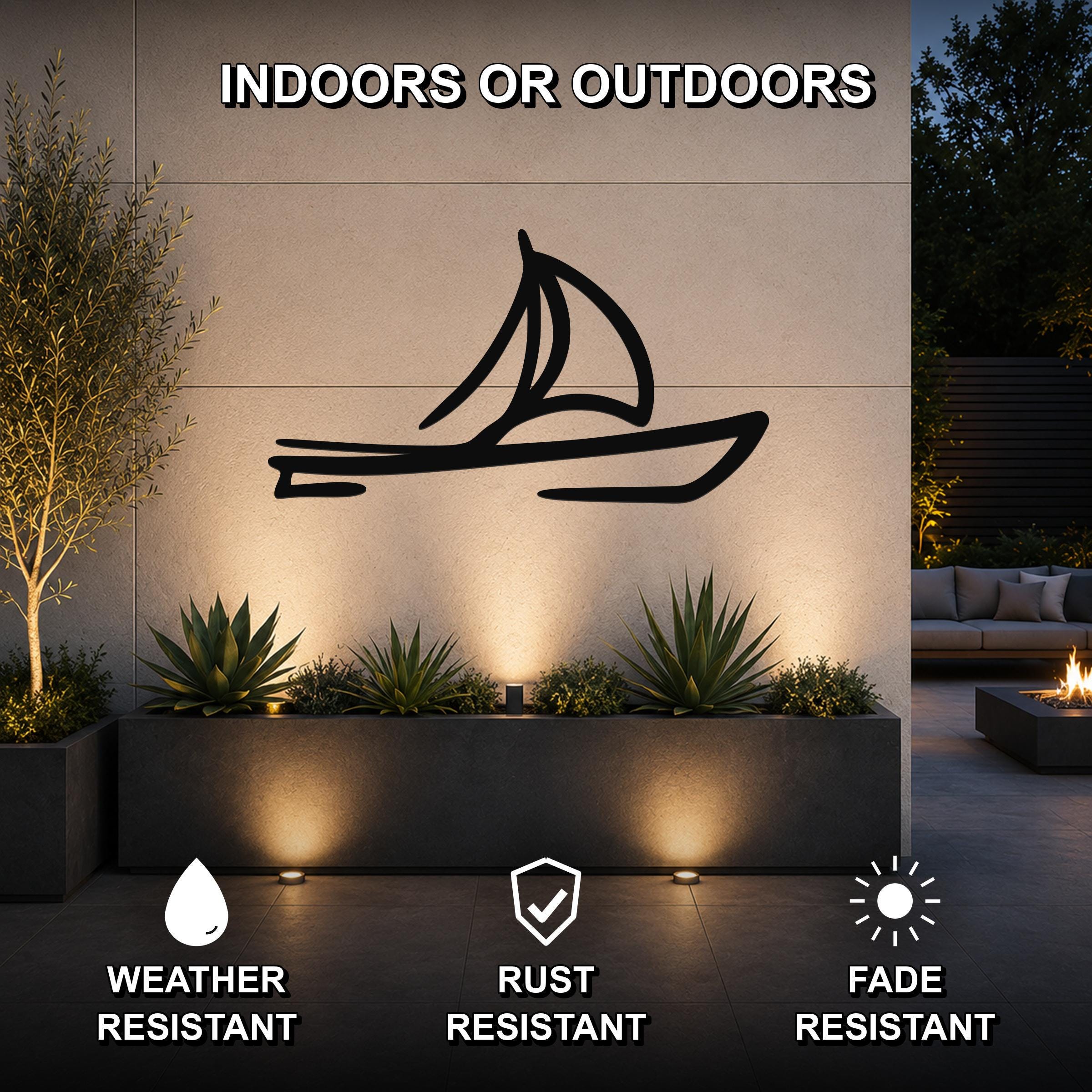 Black metal sailboat wall art silhouette mounted on an outdoor wall above a planter, illuminated by uplights in a patio setting.
