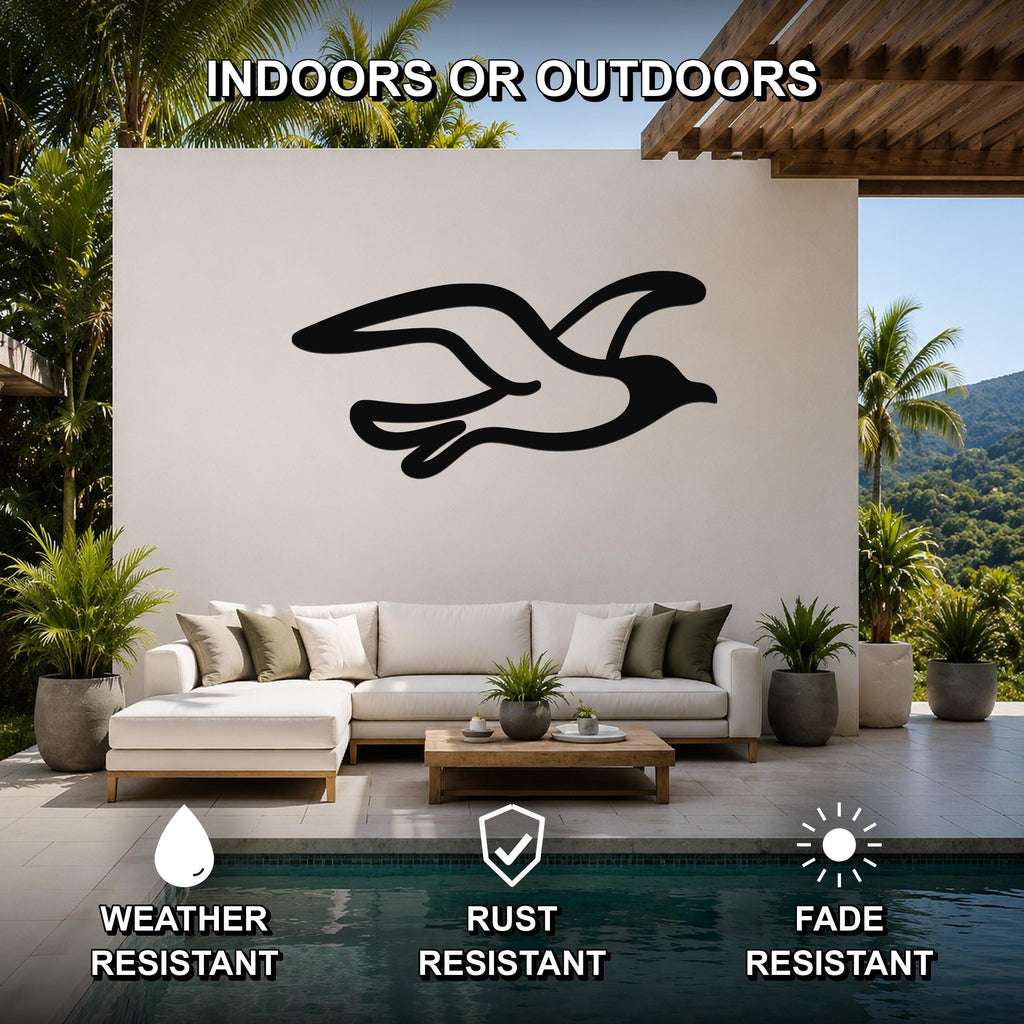 Black metal seagull wall art with motion-line cutouts, mounted on a white outdoor wall above a sofa in a patio living area.