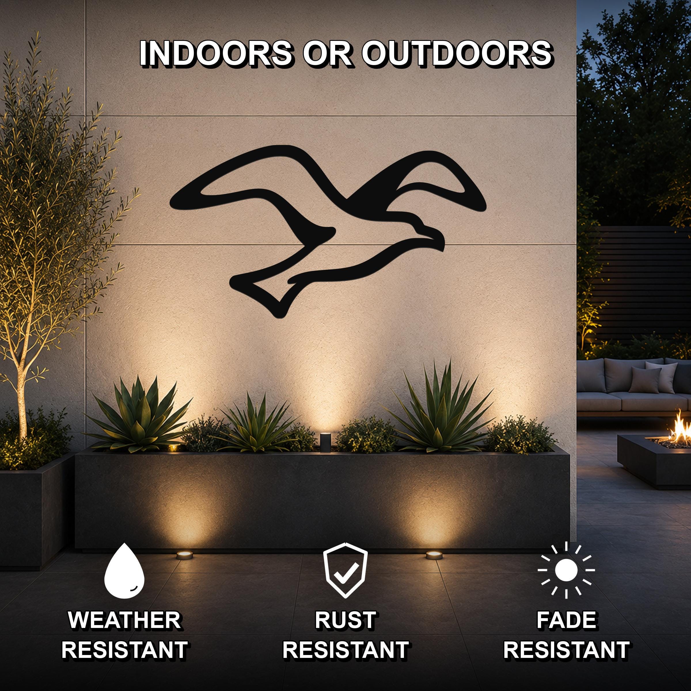 Black metal seagull wall art with motion-line cutouts, mounted on an outdoor wall above a planter in a patio setting.