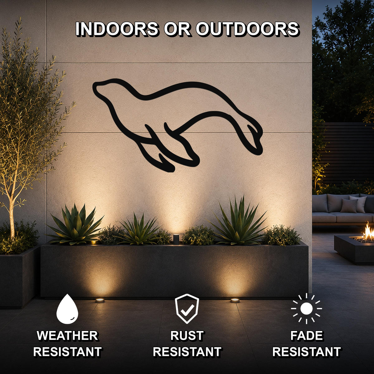 Black metal sea lion wall art silhouette mounted on an outdoor wall above a planter, illuminated by ground lights in a patio setting.