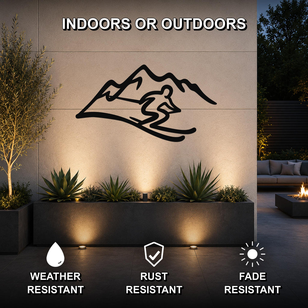 Black metal skier and mountain wall art silhouette mounted on an outdoor patio wall above a planter, with text indicating it is weather, rust, and fade resistant.