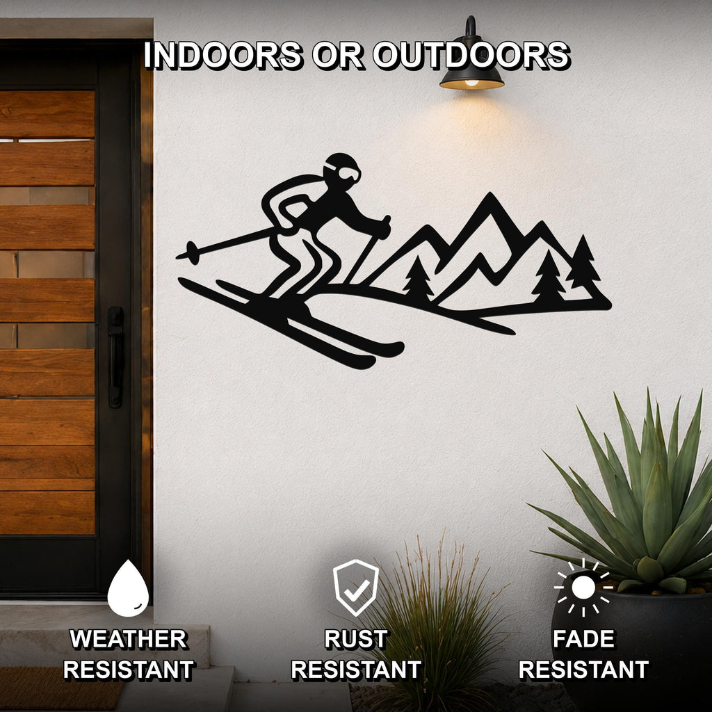 Black metal skier and mountain wall art with cutout design, mounted on an outdoor wall beside a wooden door and potted plants.