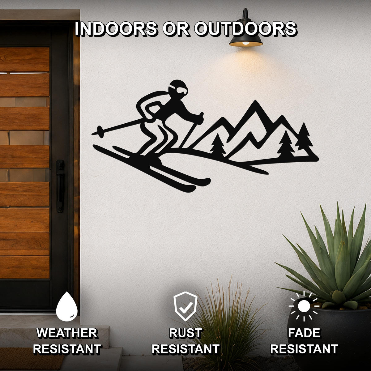 Black metal skier and mountain wall art with cutout design, mounted on an outdoor wall beside a wooden door and potted plants.