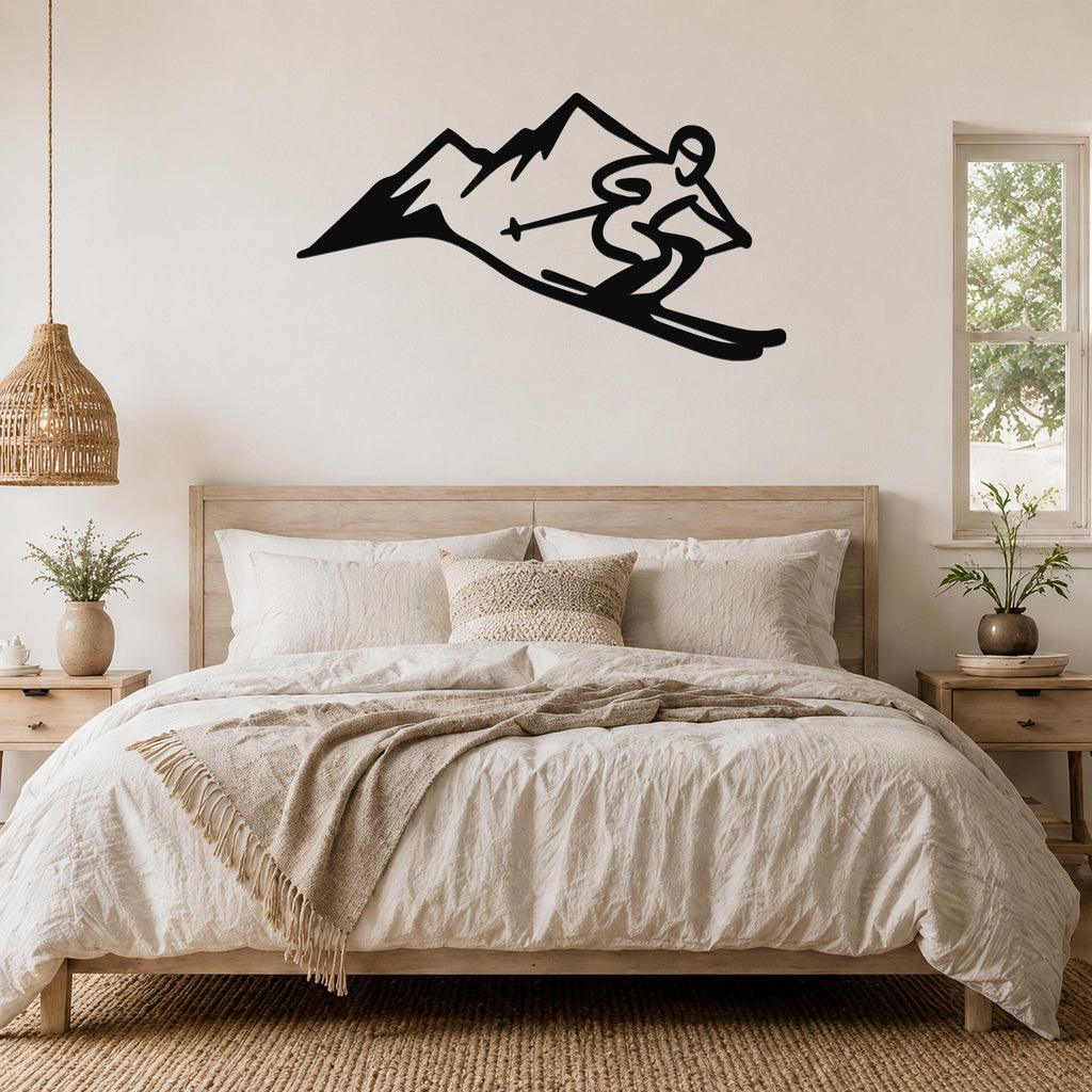Black metal wall art featuring a skier silhouette in motion above a mountain range, mounted on a bedroom wall above a wooden bed.