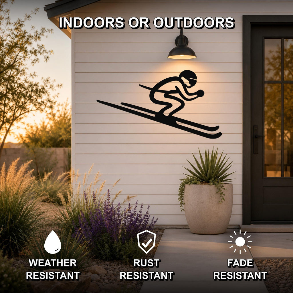 Black metal skier silhouette wall art mounted on a white siding exterior wall above a patio, with a potted plant and garden in the foreground.