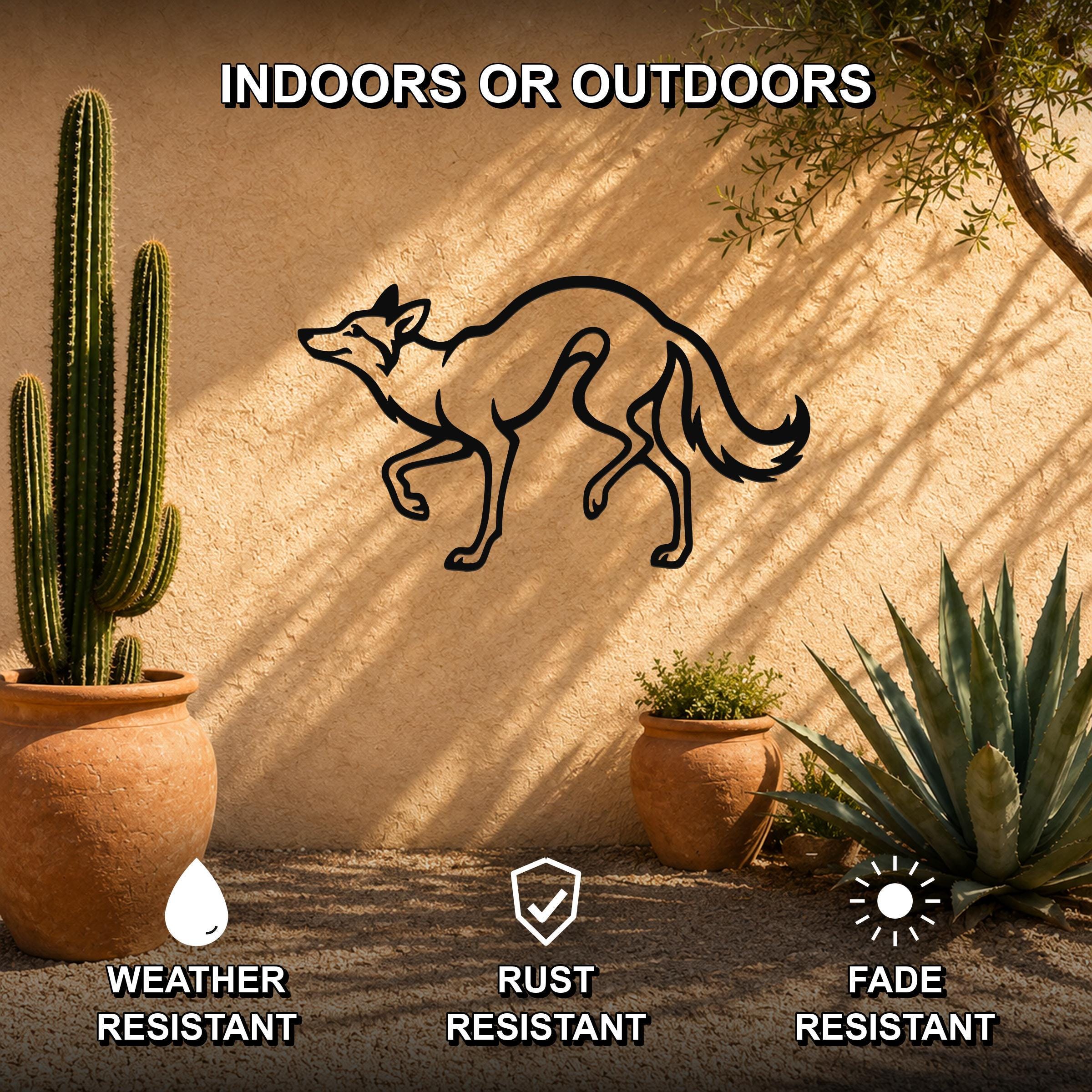 Black metal coyote silhouette wall art mounted on a stucco outdoor wall, surrounded by potted cacti and succulents in a desert-style patio setting.