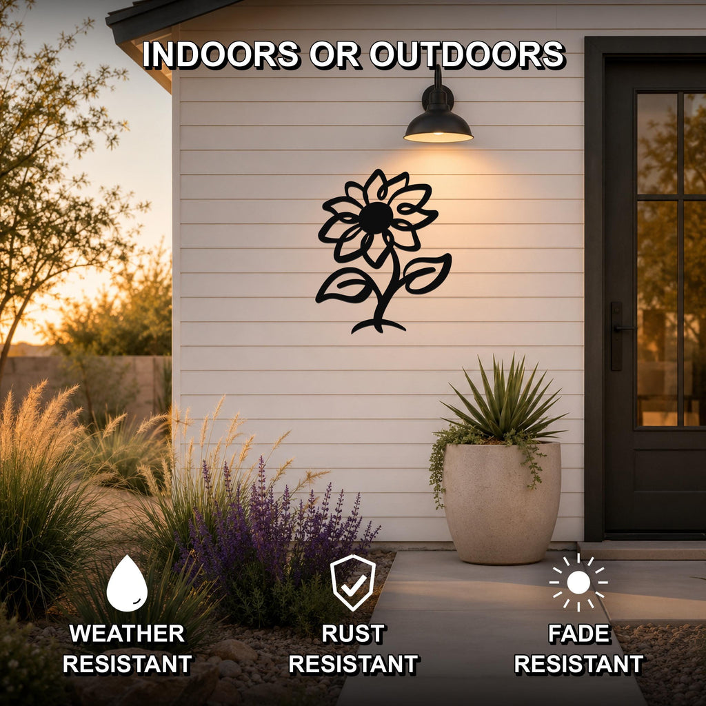 Black metal sunflower wall art with leaf and stem cutouts, mounted on a white siding exterior wall beside a door and potted plant.