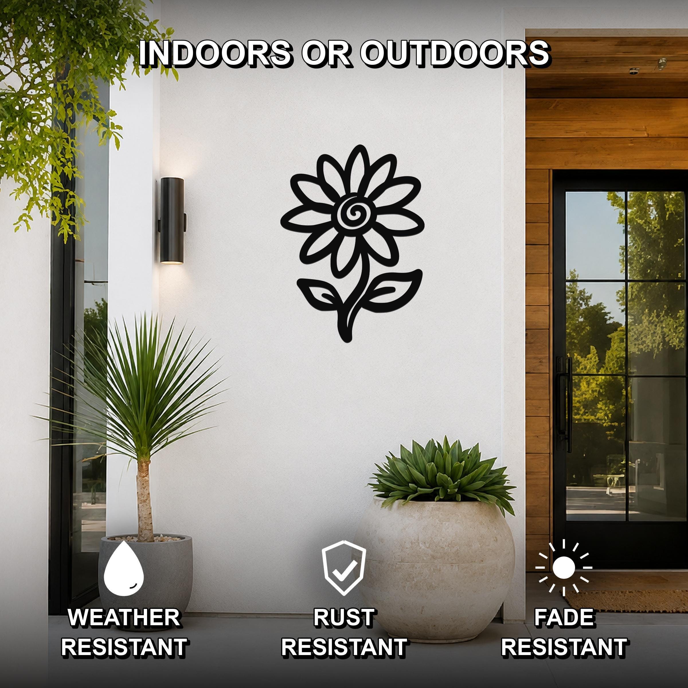 Black metal sunflower wall art silhouette with a spiral center and leaf cutouts, mounted on a white exterior wall beside a glass door and potted plants, labeled as weather, rust, and fade resistant.