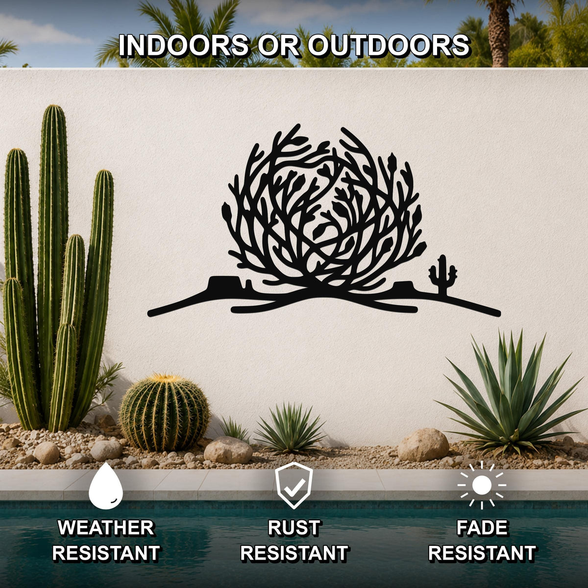Black metal tumbleweed wall art with cactus and branch cutouts, mounted on an outdoor wall above a pool in a desert garden setting.