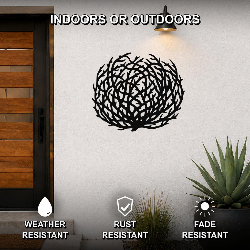 Black metal tumbleweed wall art with intricate branch cutouts, mounted on an outdoor wall beside a wooden door and potted plants.