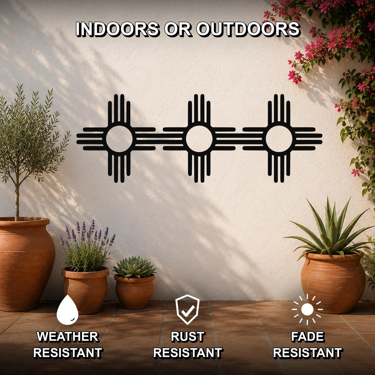 Black metal Zia Sun symbol trio wall art with cutout rays, mounted on a white outdoor wall above potted plants on a tiled patio.