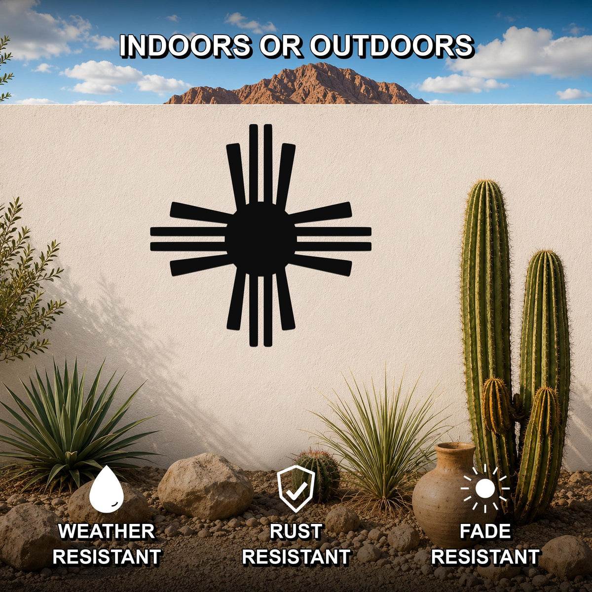 Black metal Zia Sun symbol wall art with radiating rays, mounted on an outdoor wall in a desert garden setting with cacti and rocks.