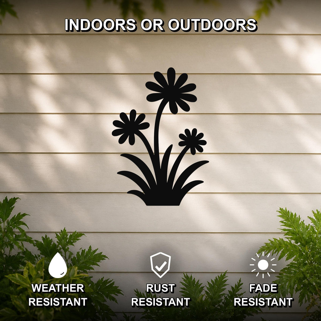 Black metal wildflower wall art with three daisy cutouts and leafy base, mounted on a beige outdoor wall with greenery, weather, rust, and fade resistant.