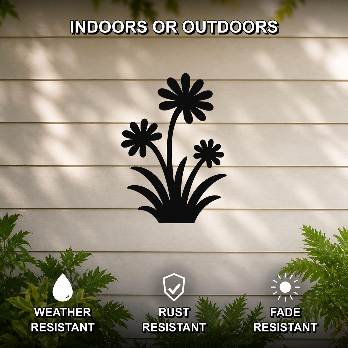 Black metal wildflower wall art with three daisy cutouts and leafy base, mounted on a beige outdoor wall with greenery, weather, rust, and fade resistant.