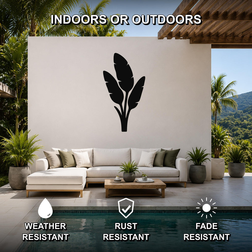 Black metal tropical leaves wall art silhouette mounted on a white outdoor wall above a sofa in a patio setting, weather resistant, rust resistant, and fade resistant.