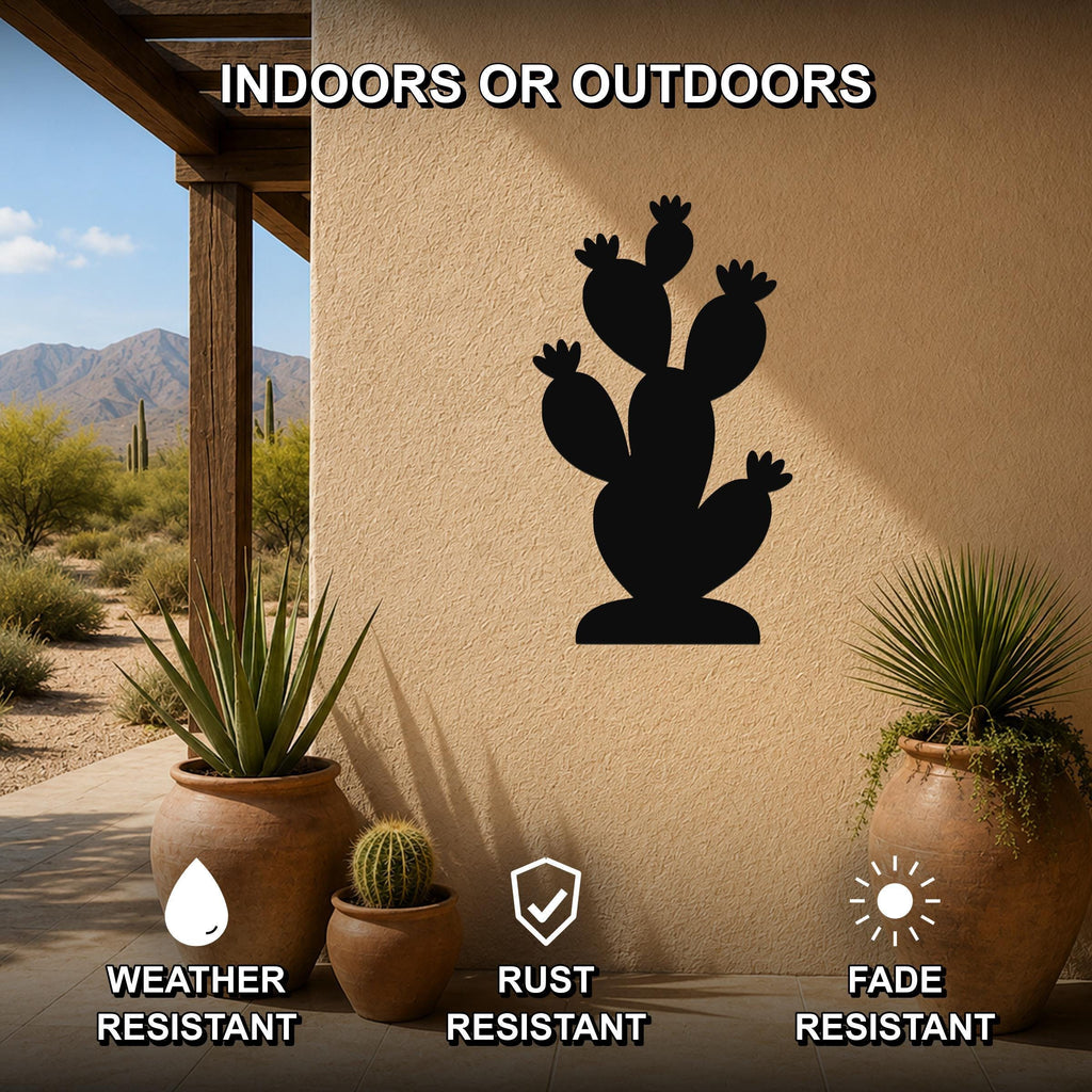Black metal prickly pear cactus wall art silhouette mounted on a beige outdoor wall, displayed on a patio with potted plants and desert scenery in the background.