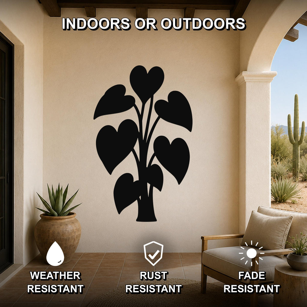 Black metal wall art in the silhouette of a philodendron with heart-shaped leaves, mounted on a beige outdoor patio wall above a wooden chair and potted plant.