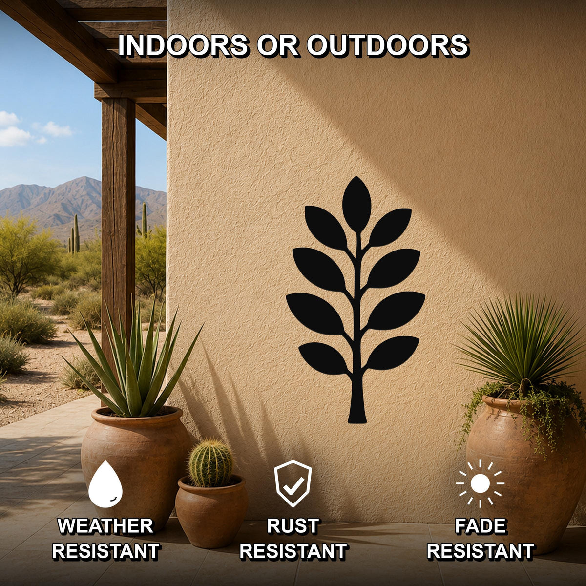 Black metal olive branch wall art silhouette mounted on a beige outdoor wall, displayed on a patio with potted plants and desert scenery in the background.