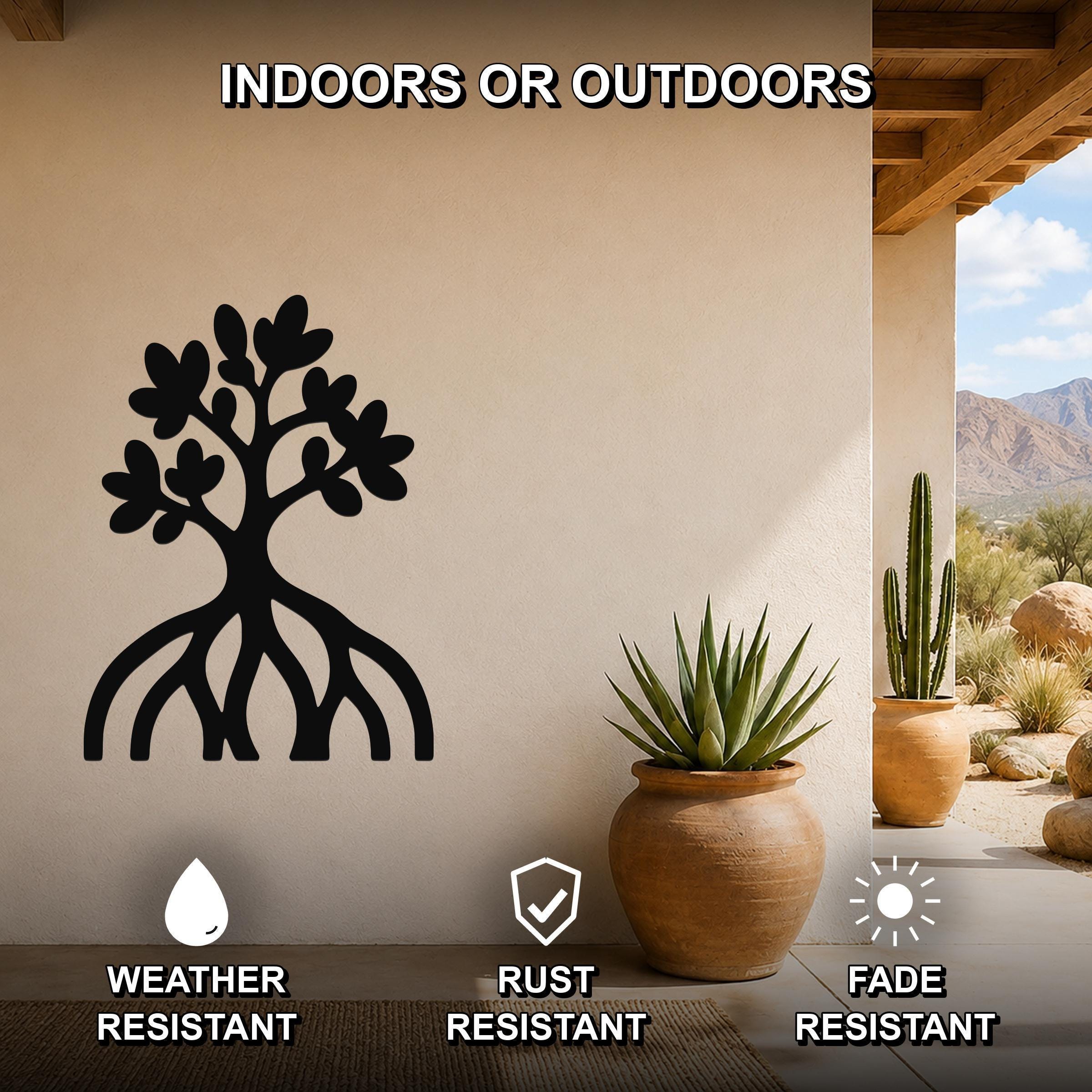 Black metal wall art in the silhouette of a tree with visible roots and leafy branches, mounted on a beige outdoor wall beside potted plants and a desert landscape view.
