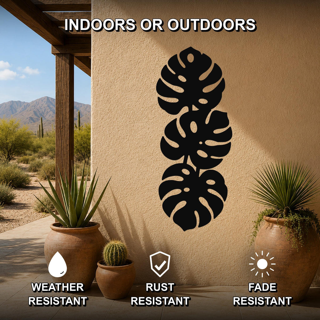 Black metal monstera leaf wall art with three stacked leaf cutouts, mounted on an outdoor patio wall between potted plants.