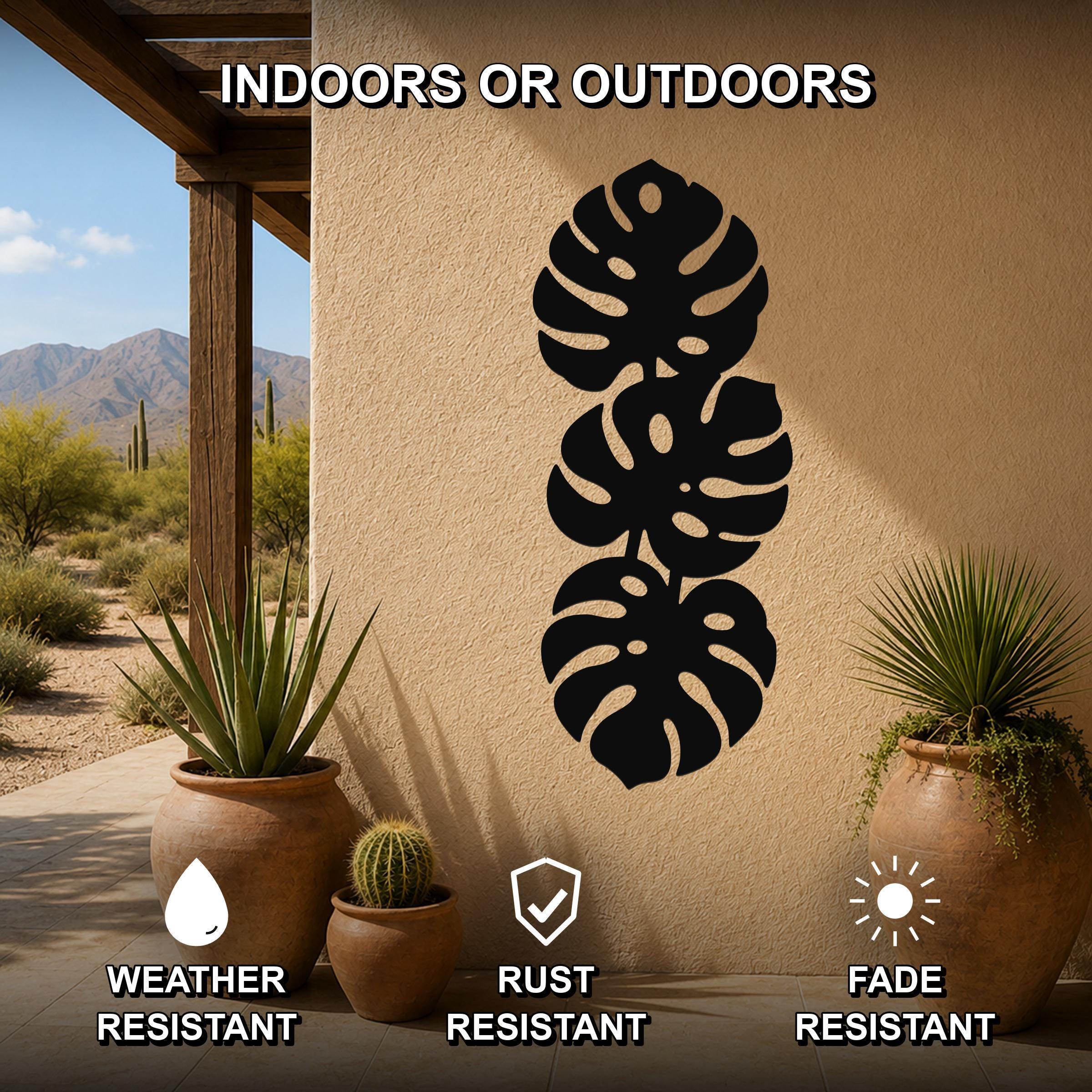Black metal monstera leaf wall art with three stacked leaf cutouts, mounted on an outdoor patio wall between potted plants.
