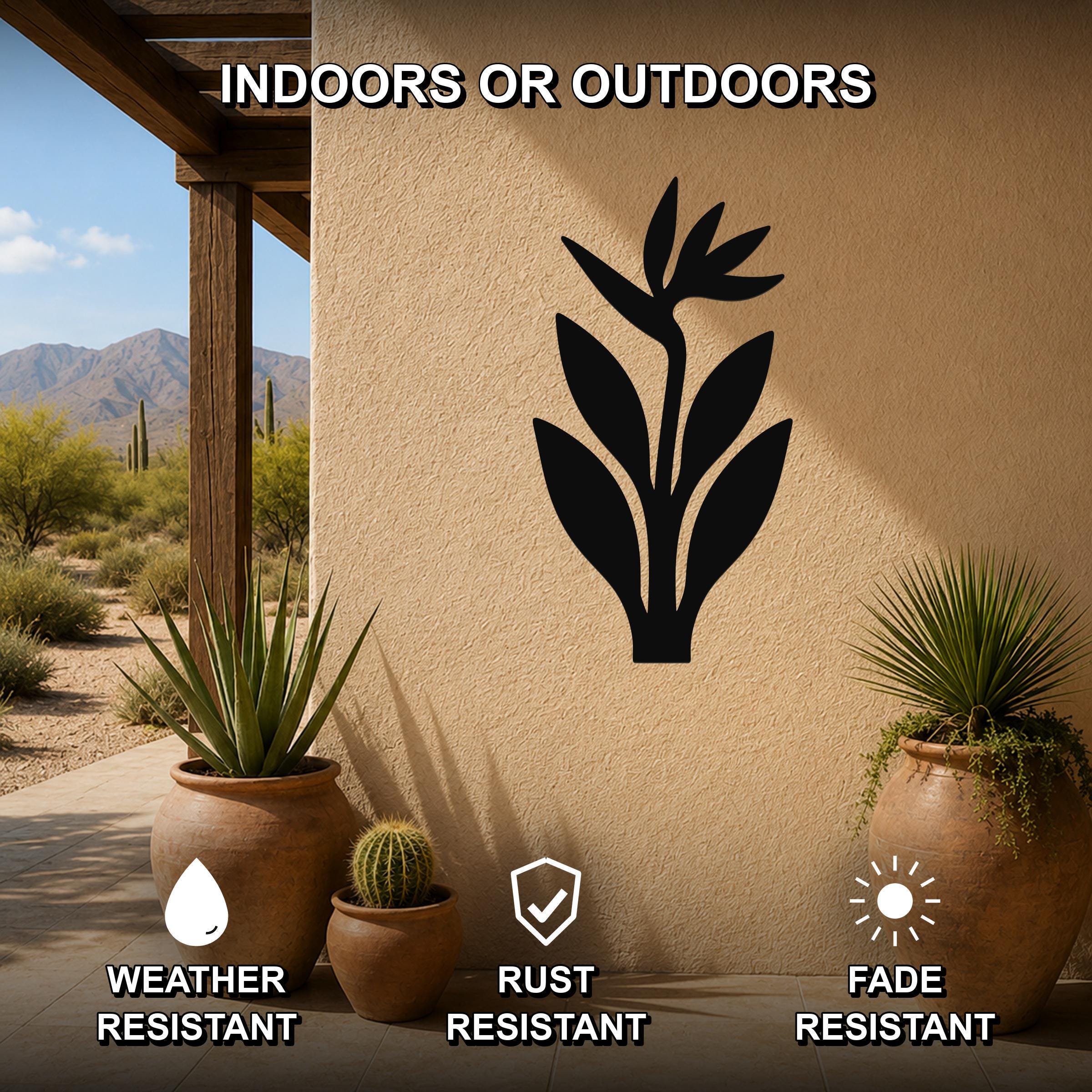 Black metal Bird of Paradise wall art silhouette mounted on an outdoor stucco wall, displayed above potted plants on a patio with desert scenery in the background.