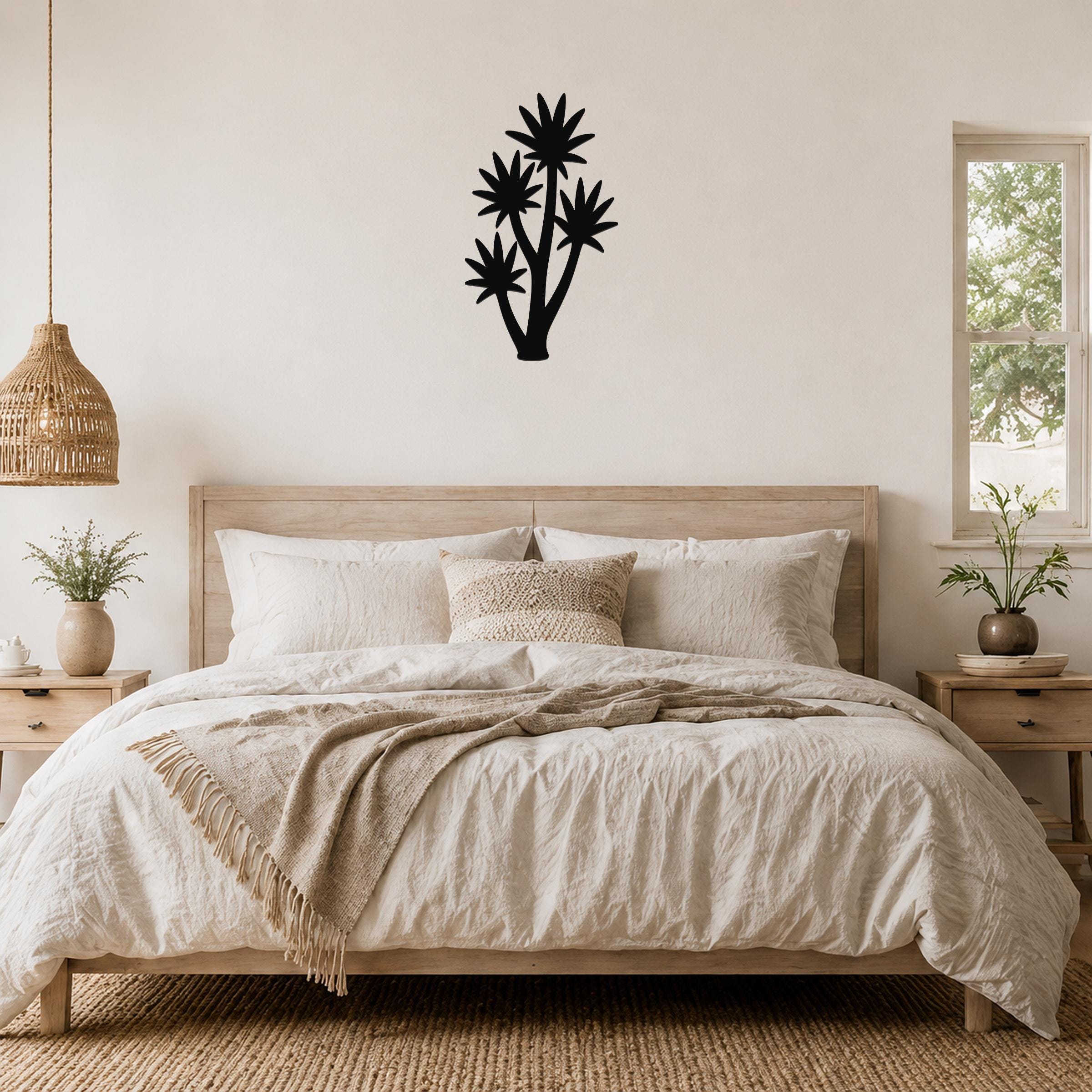 Black metal wall art in a tall yucca silhouette with multiple star-shaped leaf cutouts, mounted above a wooden bed in a neutral bedroom.