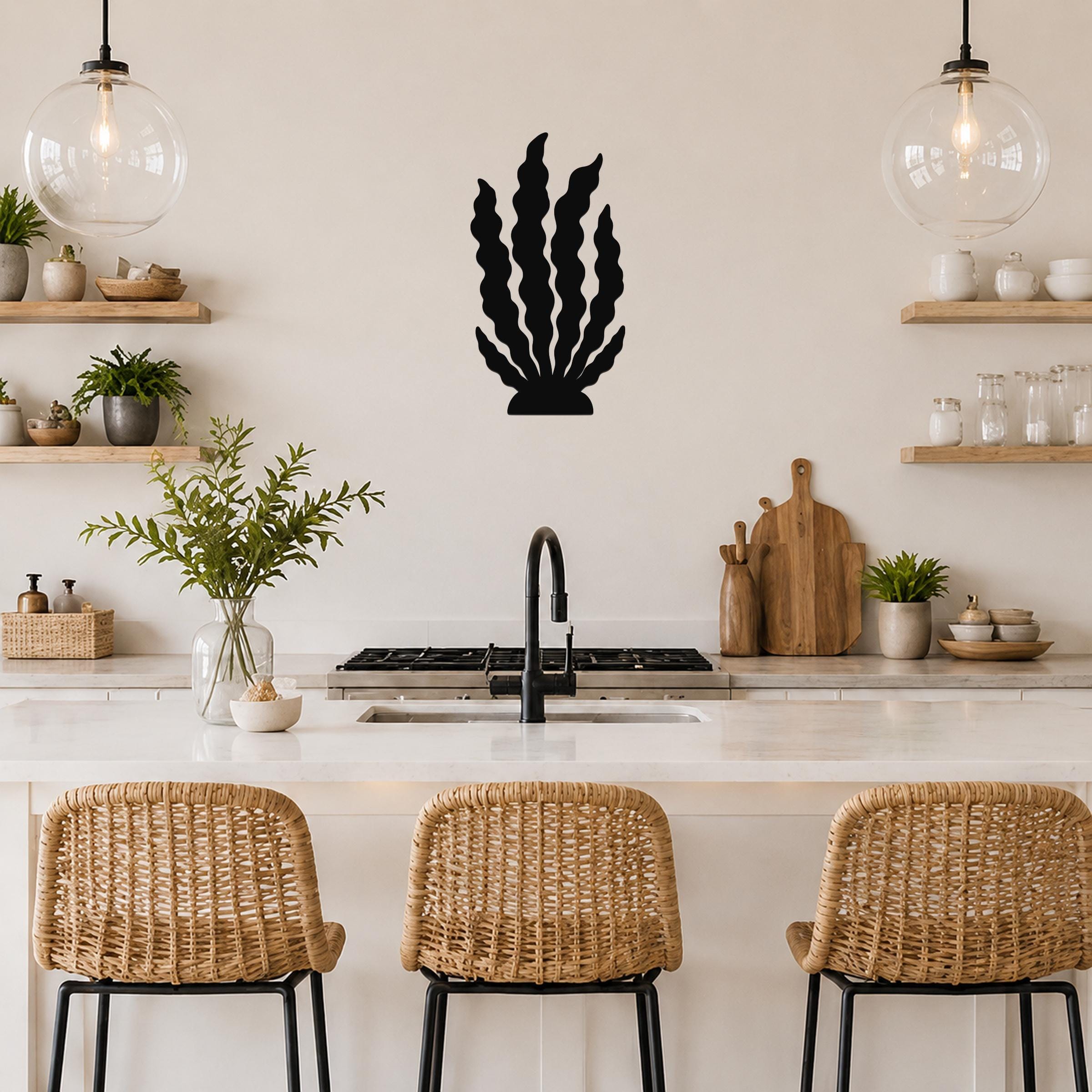 Black metal kelp wall art with wavy leaf cutouts, mounted on a kitchen wall above a counter between two glass pendant lights.