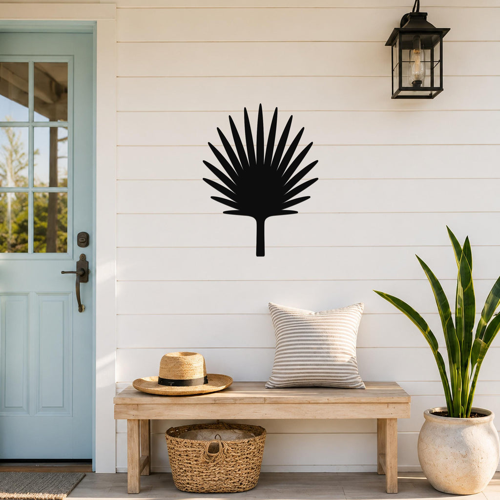 Black metal fan palm tree wall art silhouette mounted on a white shiplap wall above a wooden bench in a porch entryway.