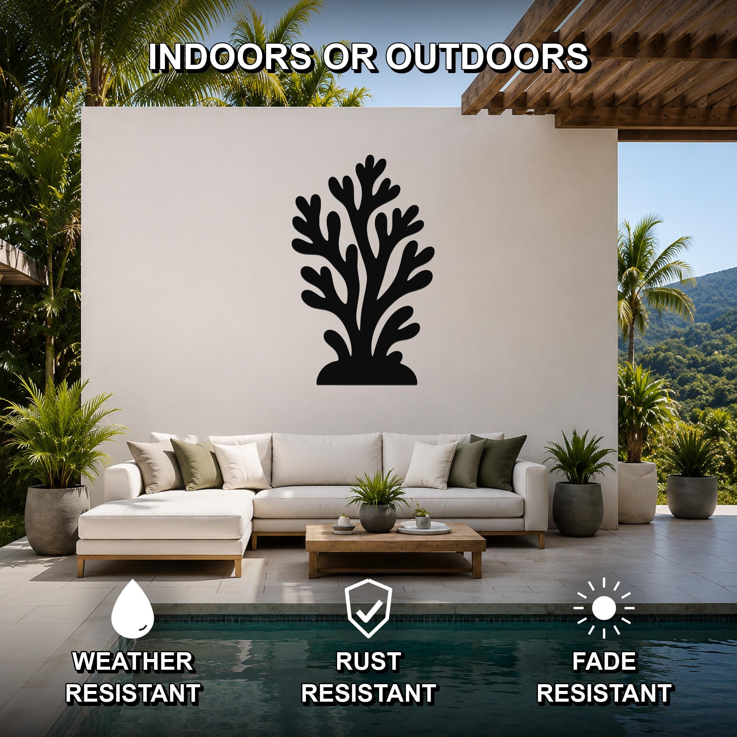 Black metal coral wall art with branching cutouts, mounted on a white outdoor wall above a sofa in a patio setting near a pool.