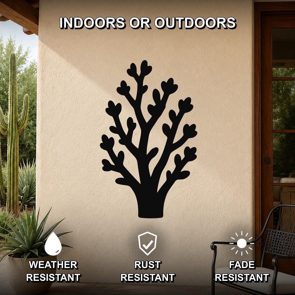 Black metal wall art in a tree silhouette with branching cutouts, mounted on an outdoor patio wall with cacti and a chair visible nearby.
