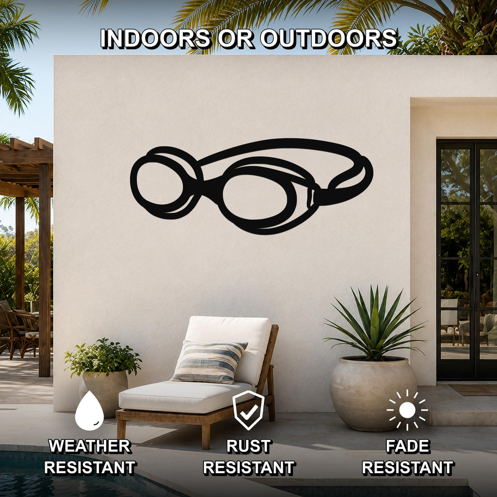 Black metal swim goggles wall art with a bold silhouette design, mounted on an outdoor patio wall near a lounge chair and pool.