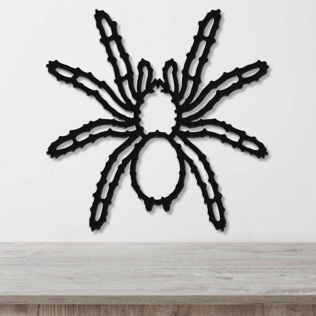 Black metal spider wall art with intricate leg cutouts, mounted on a white wall above a light wood surface.