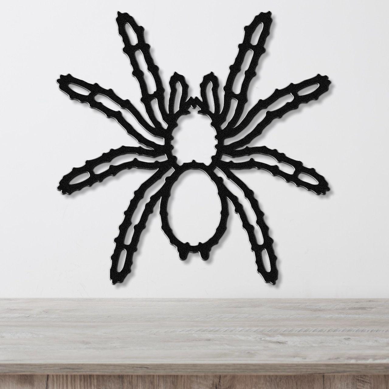 Black metal spider wall art with intricate leg cutouts, mounted on a white wall above a light wood surface.