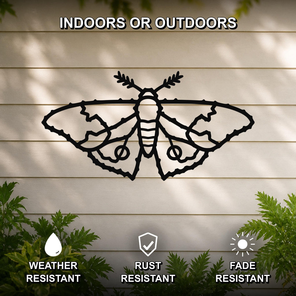 Black metal moth wall art with detailed wing cutouts, mounted on a light-colored outdoor wall with greenery, weather resistant, rust resistant, and fade resistant.