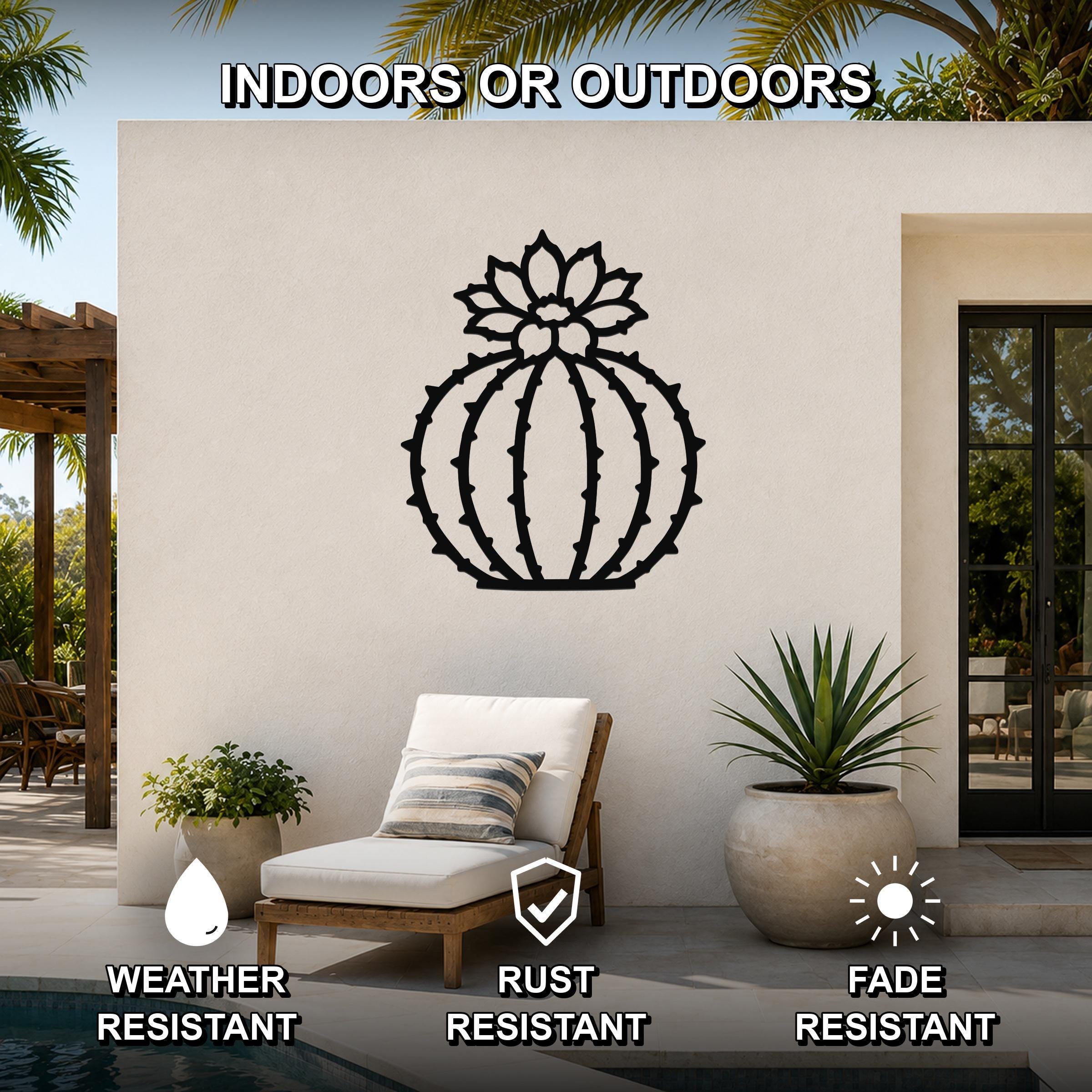 Black metal barrel cactus wall art with flower and spine cutouts, mounted on an outdoor patio wall above a lounge chair.