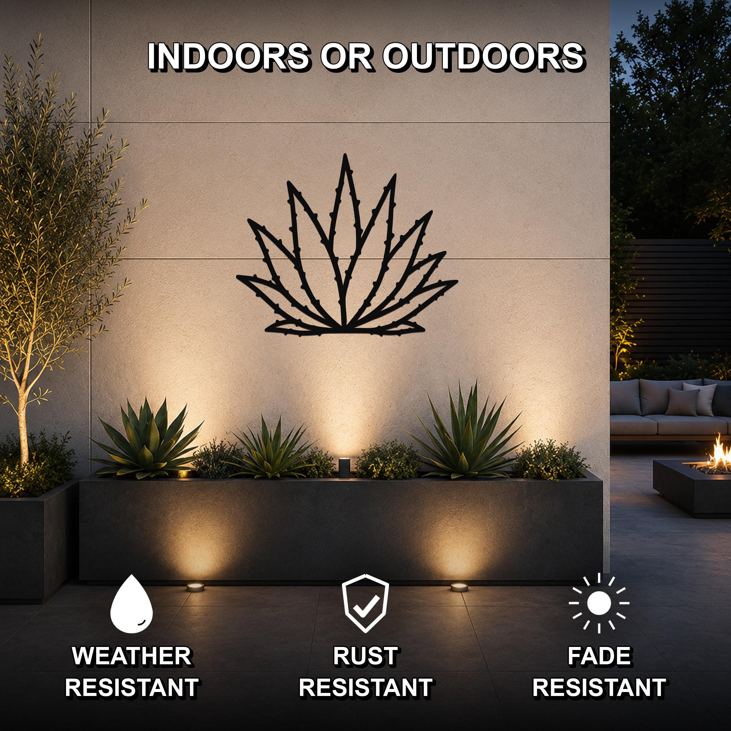 Black metal agave wall art with spiky leaf cutouts, mounted on an outdoor wall above a planter in a modern patio setting.