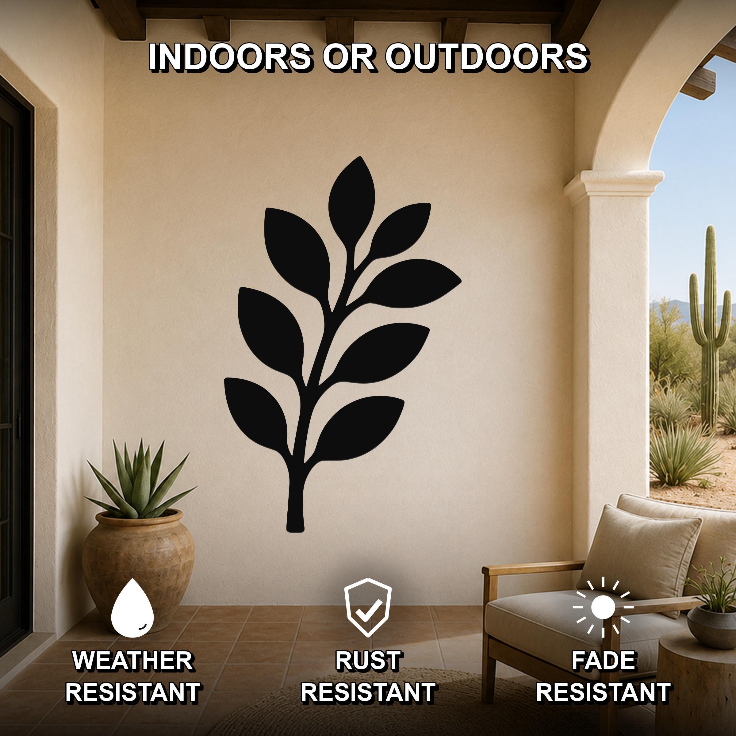 Black metal olive branch wall art with leaf cutouts, mounted on a beige outdoor patio wall above a wooden chair and potted succulent.