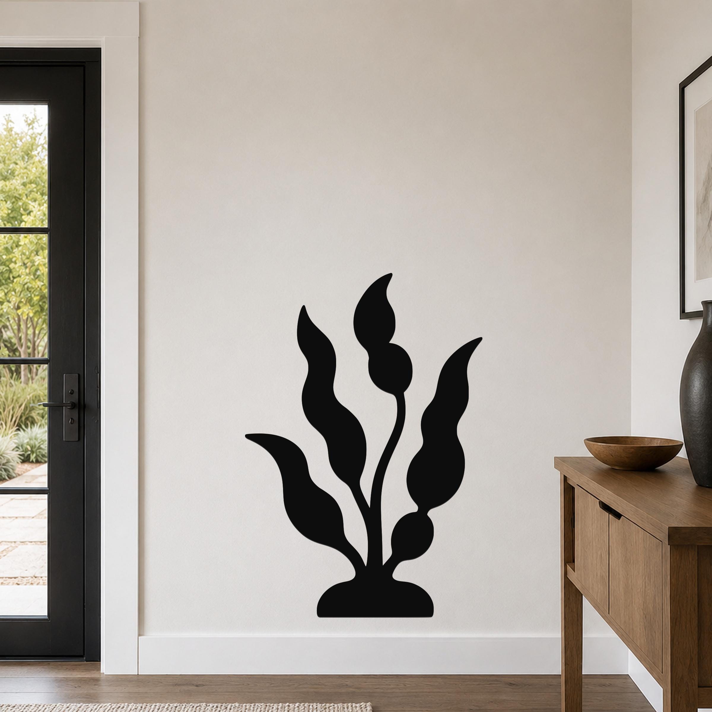 Black metal wall art in a kelp or seaweed silhouette design, mounted on a light-colored wall in a modern entryway near a door and console table.