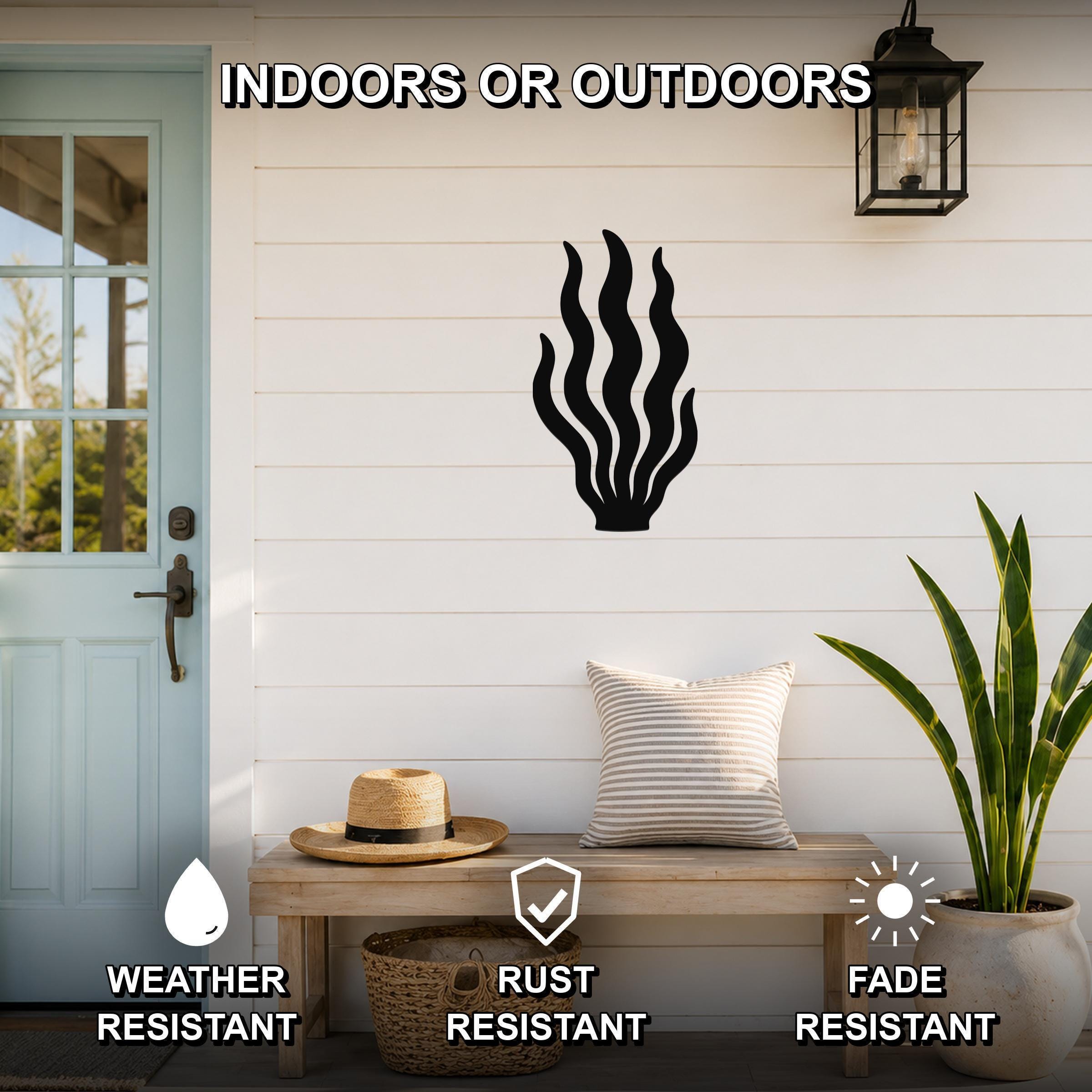 Black metal kelp wall art with flowing frond cutouts, mounted on a white shiplap wall above a wooden bench on a porch.
