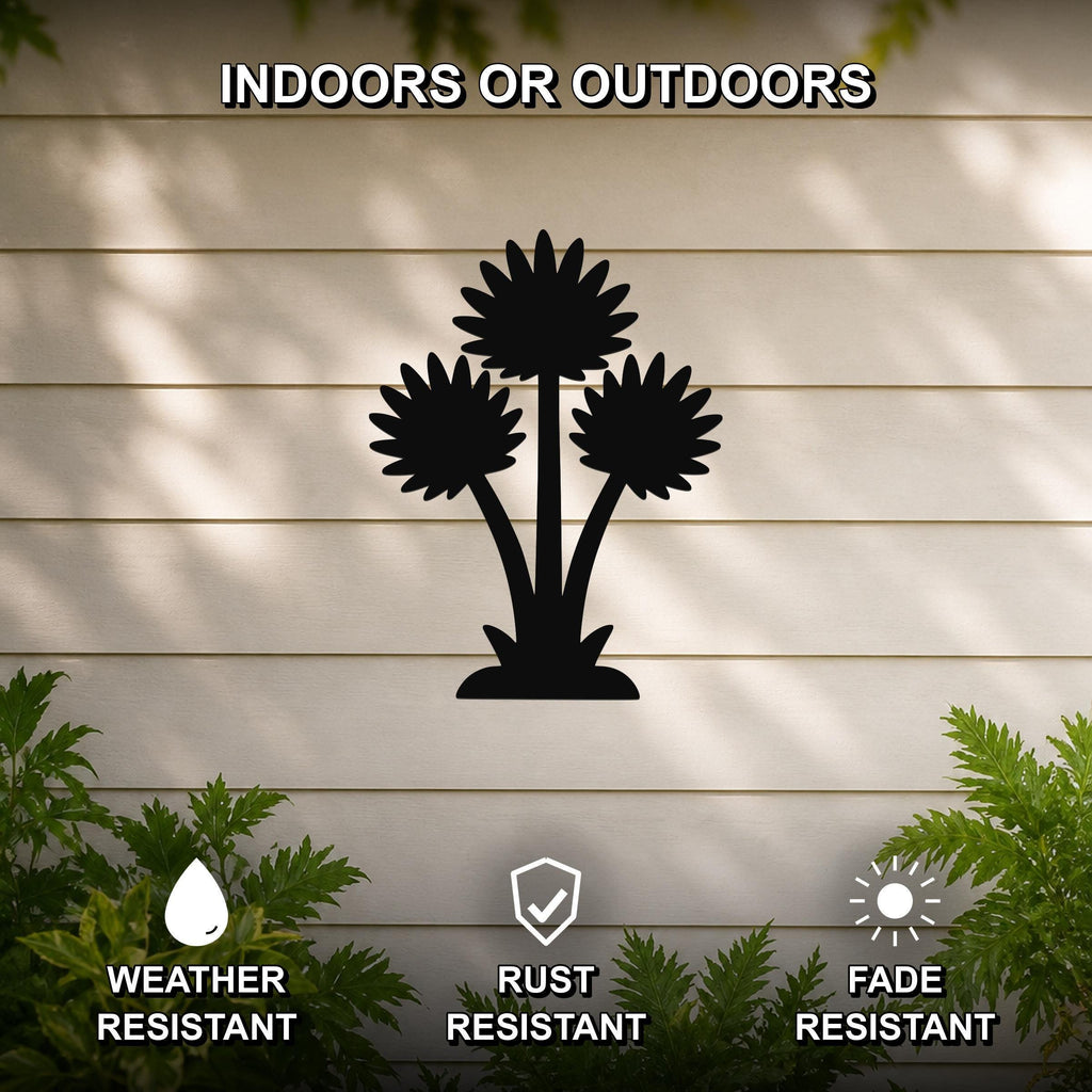 Black metal wall art featuring a silhouette of three wildflowers, mounted on a beige outdoor wall with greenery below, weather resistant, rust resistant, and fade resistant.